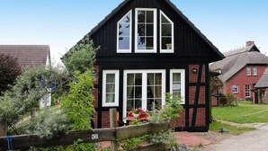 A black and white Tudor-style house with a steeply pitched roof, a central chimney, and a small garden with a wooden fence. - Holiday Home Haffschein, Monkebude (Monkebude)