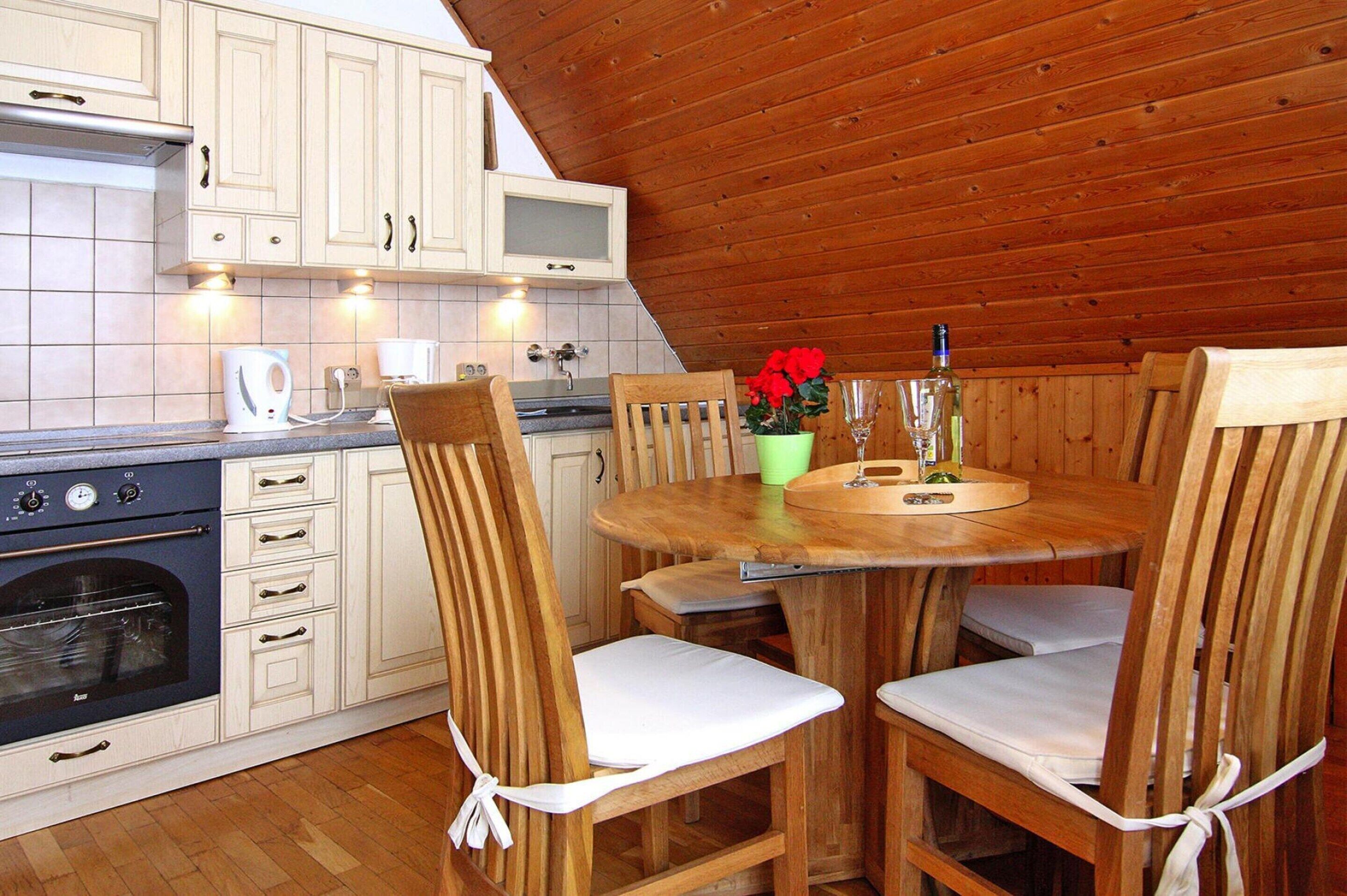 Un intérieur en bois avec une cuisine équipée de meubles blancs, d’une cuisinière et d’une table à manger avec des chaises.