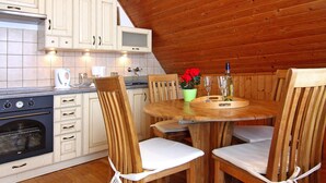 A wooden interior with a kitchen featuring white cabinets, a stove, and a dining table with chairs. - Holiday Home Haffschein, Monkebude (Monkebude)