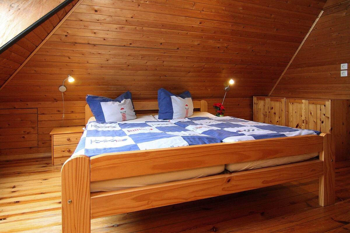 A wooden bunk bed in a cabin with a sloped ceiling, a nightstand, and two wall-mounted lamps.
