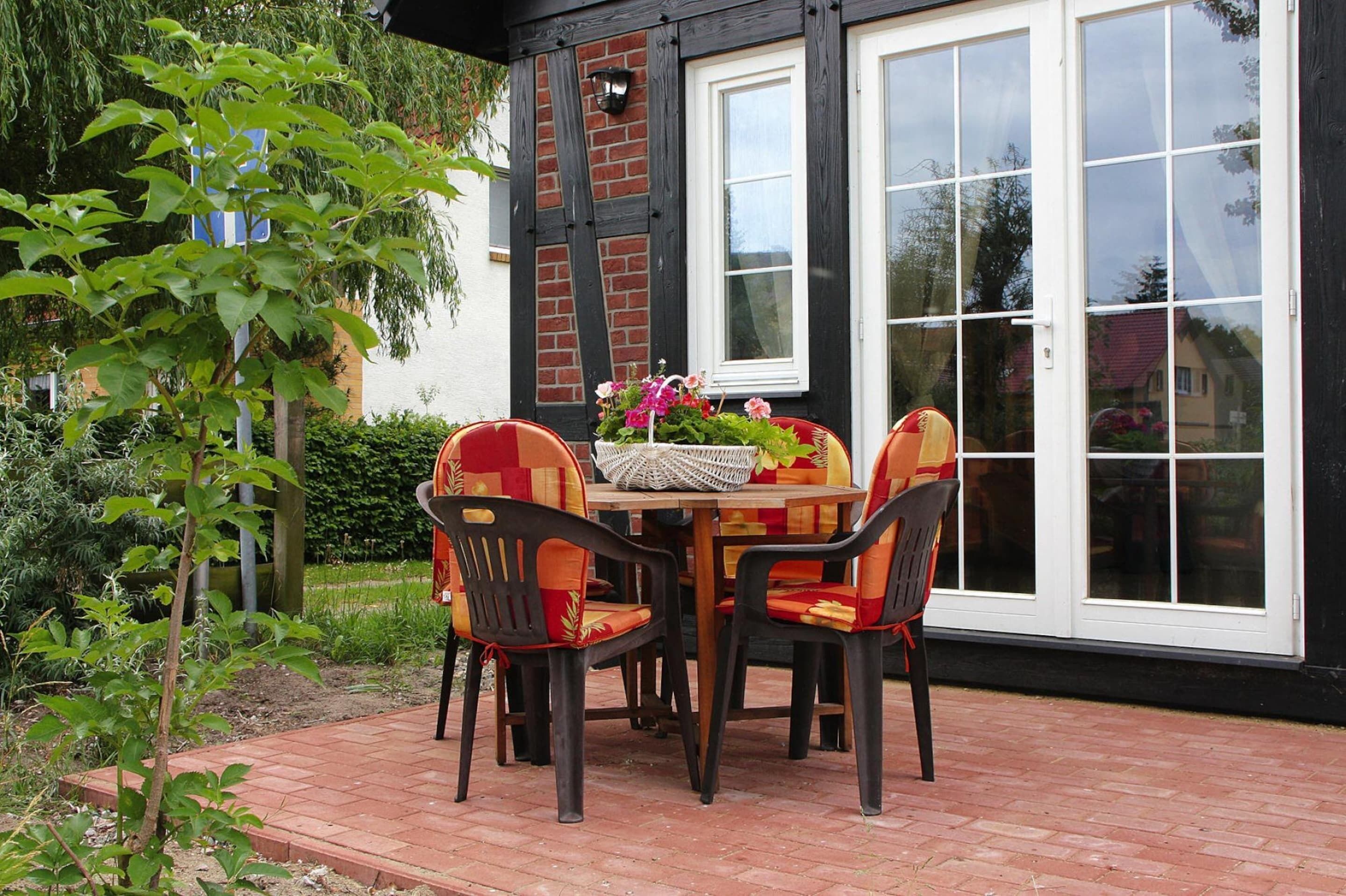 A patio with a table and chairs, a potted plant, and a house with a black and white exterior.