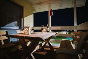 An outdoor dining area with wooden benches and tables, a candle holder, and a bottle of wine.