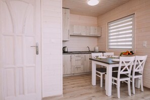 A compact kitchen with wooden cabinets, a sink, and a dining area with a table and chairs. - Family Holiday Resort, Holiday Houses, Bobolin (Darlowo)