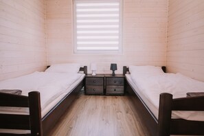 A small, cozy room with two single beds, a window with blinds, and a nightstand with a lamp between the beds. - Family Holiday Resort, Holiday Houses, Bobolin (Darlowo)