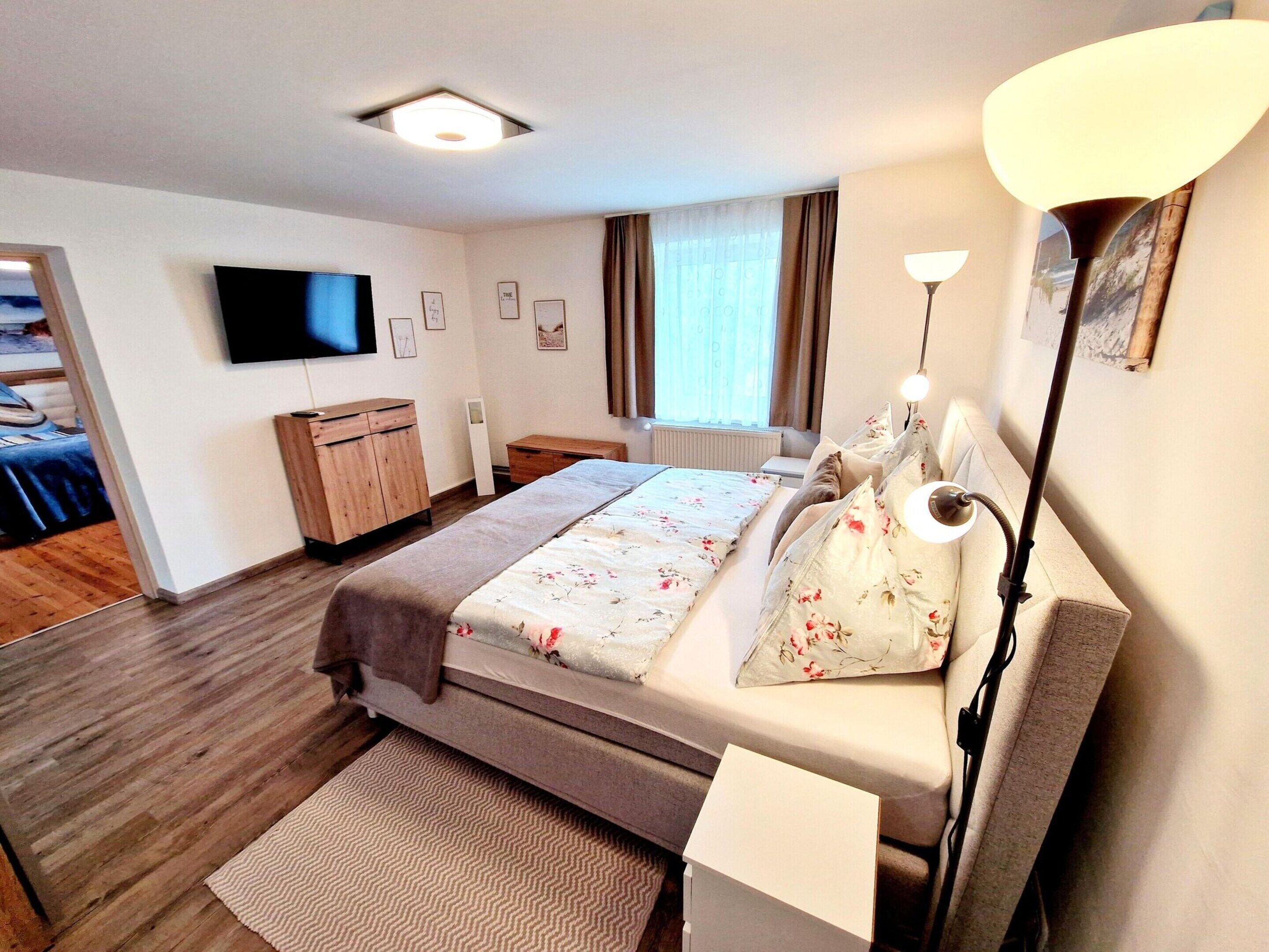 A hotel room with a bed, bedside table, lamp, and a TV on the wall.