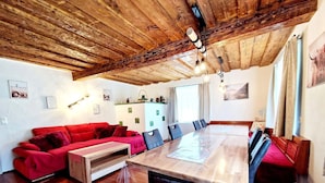 A cozy room with a wooden ceiling, a red sofa, a dining table, and a kitchen area with a fridge and cabinets.
