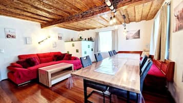 Une pièce chaleureuse avec un plafond en bois, un canapé rouge, une table à manger et un coin cuisine équipé d’un réfrigérateur et de placards.