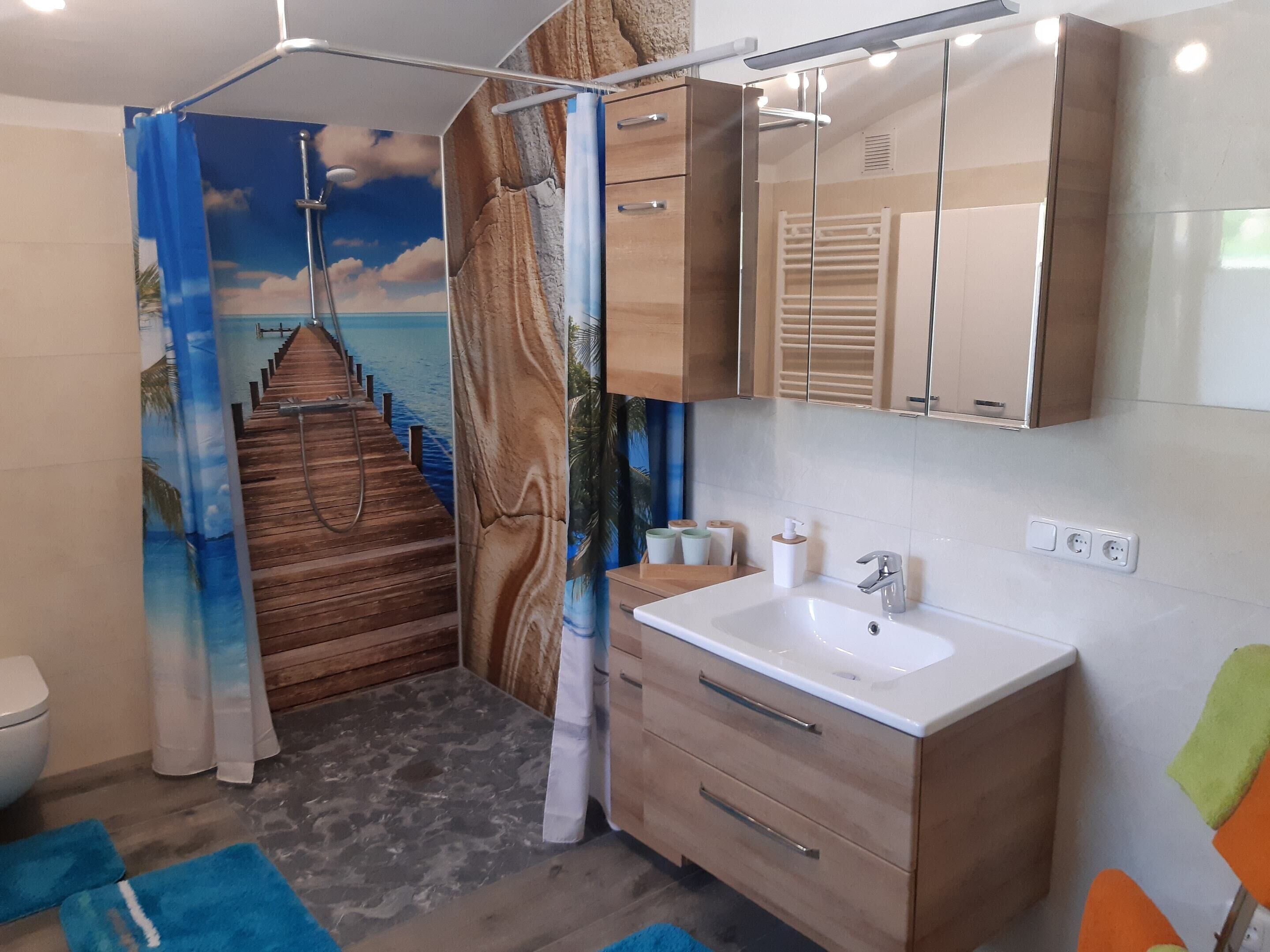 Ein Badezimmer mit Holzboden, einem weißen Waschbecken, einem Spiegel und einer Duschvorhang mit Strandmotiv.