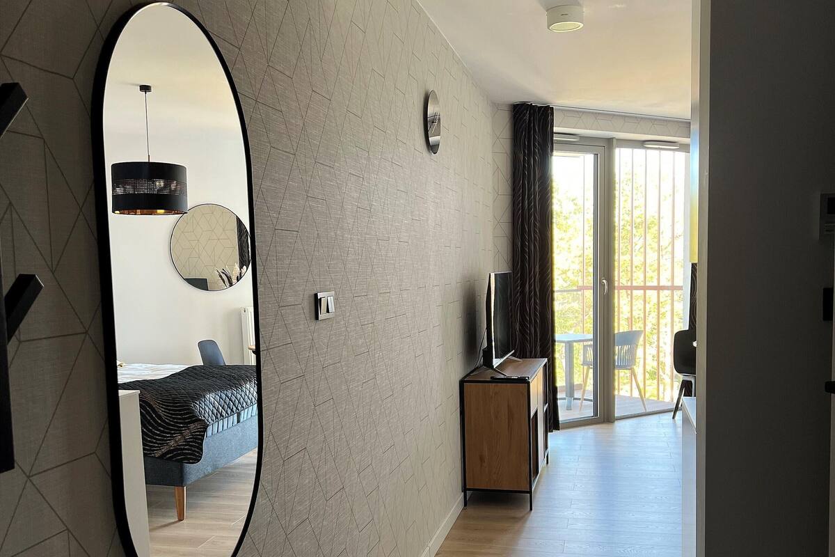 A modern living room with a large mirror, a sofa, a TV, and a wooden cabinet.
