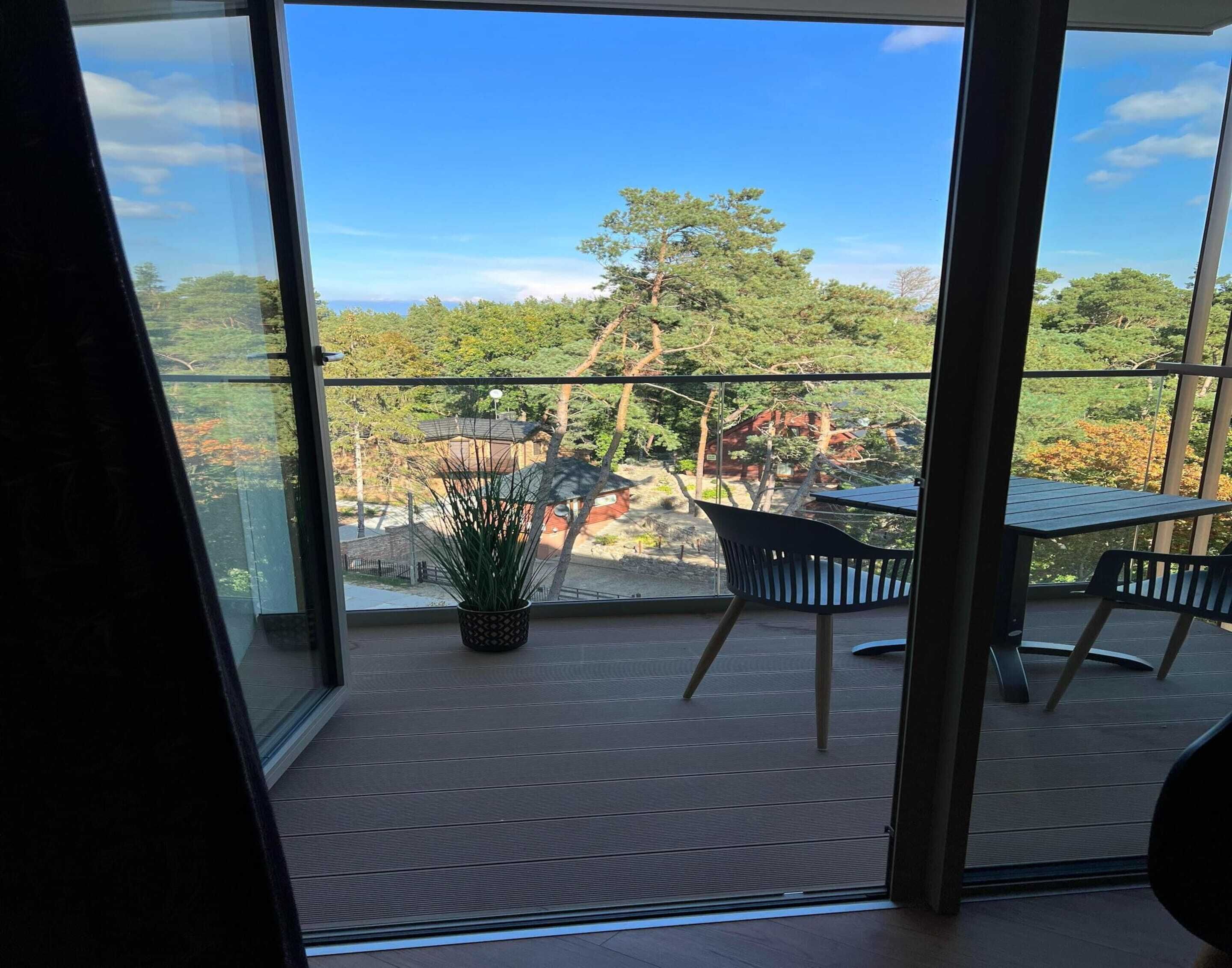 Ein Balkon mit Blick auf Bäume und ein Gebäude. Ein Blumentopf und zwei Stühle sind vorhanden.
