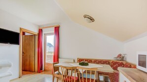 A cozy room with a wooden floor, a dining table with chairs, a sofa with red cushions, and a wooden cabinet. - Apartment in Hainzenberg in a ski Area (Hainzenberg)