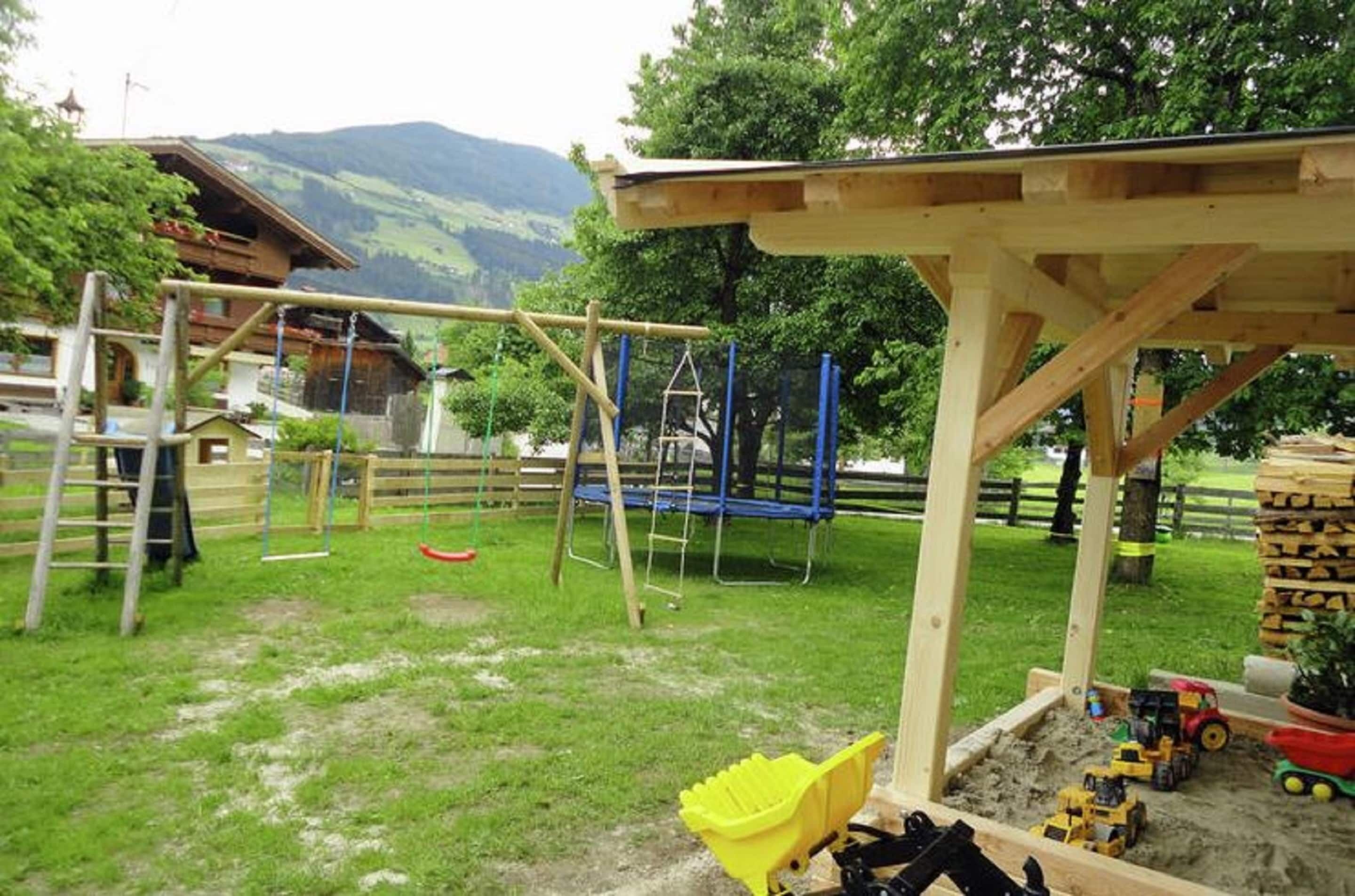 Un parque infantil con columpios, un trampolín y un arenero lleno de vehículos de juguete.