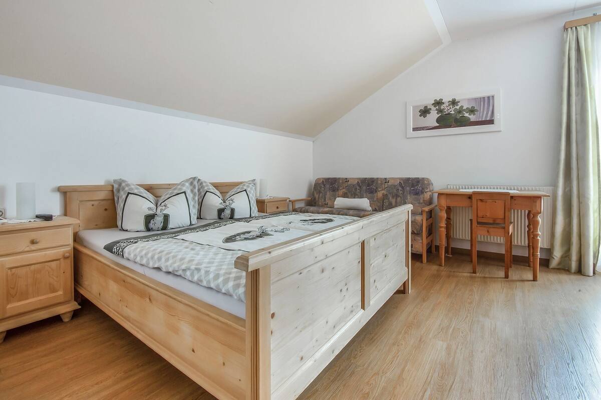 A bedroom with a wooden bed, a nightstand, a desk, and a chair.