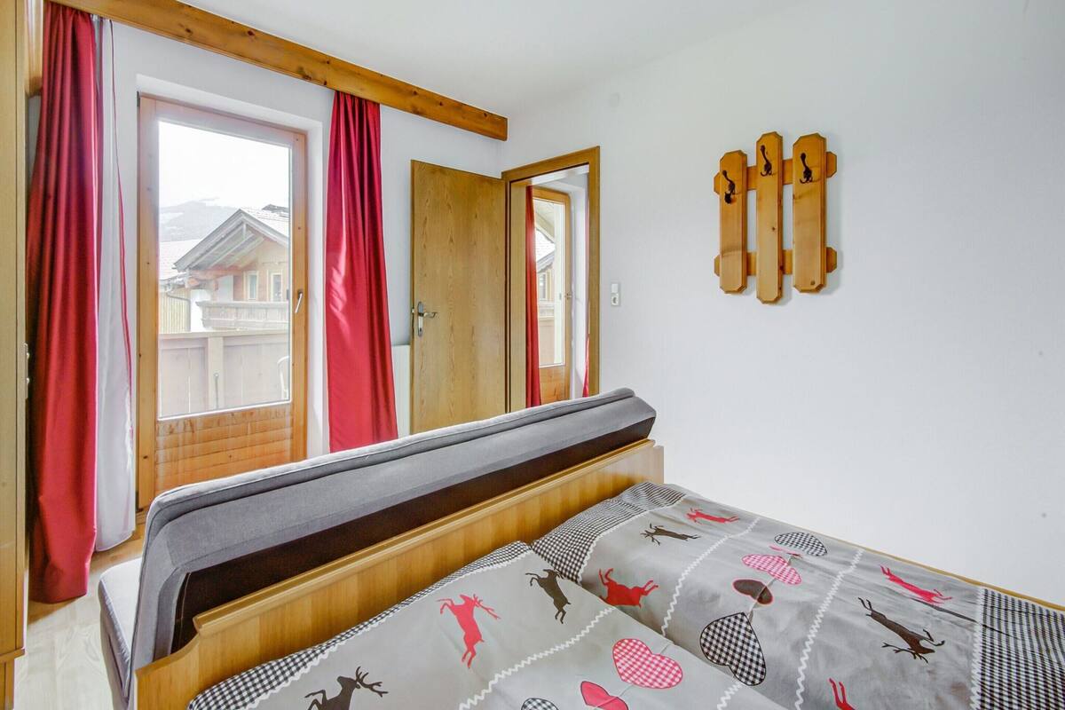 Une chambre à coucher avec un lit, une tête de lit en bois, une fenêtre avec des rideaux rouges et une porte.