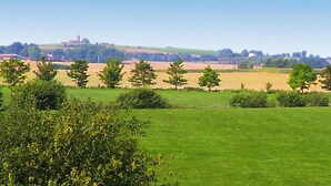 A rural landscape with fields, trees, and a distant building on a hill.