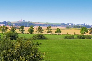 Paisaje rural con campos, árboles y una construcción distante en una colina.