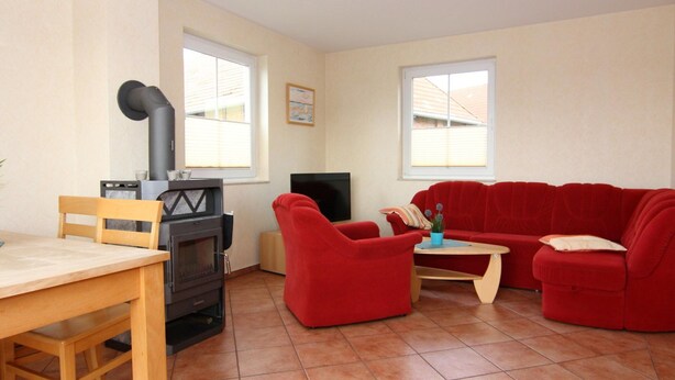 A living room with a fireplace, a TV, a red sofa, and a wooden table. - Semi-detached House, Kuehlungsborn (Kuehlungsborn)