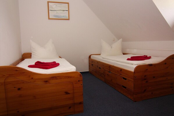 Two wooden beds with white bedding and red towels, in a room with a sloped ceiling and a framed picture on the wall. - Semi-detached House, Kuehlungsborn (Kuehlungsborn)