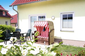 A patio area with outdoor furniture, including a table and chairs, and a wicker chair with a striped cover. - Semi-detached House, Kuehlungsborn (Kuehlungsborn)