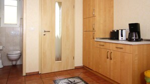 A small kitchen with wooden cabinets, a coffee maker, and a toilet visible in the adjacent bathroom.