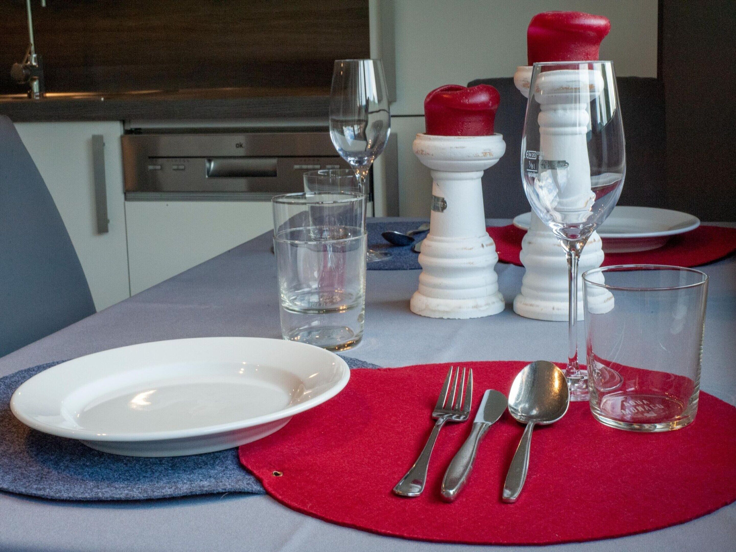 A dining table set with a white plate, two glasses, a red napkin, and silver cutlery.