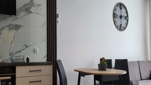 A modern kitchen with a marble backsplash, a built-in oven, and a dining area with a round table and chairs. - Comfy Apartment Near the sea in Gaski (Mielno)