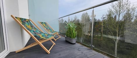 A balcony with two wooden lounge chairs and a potted plant.