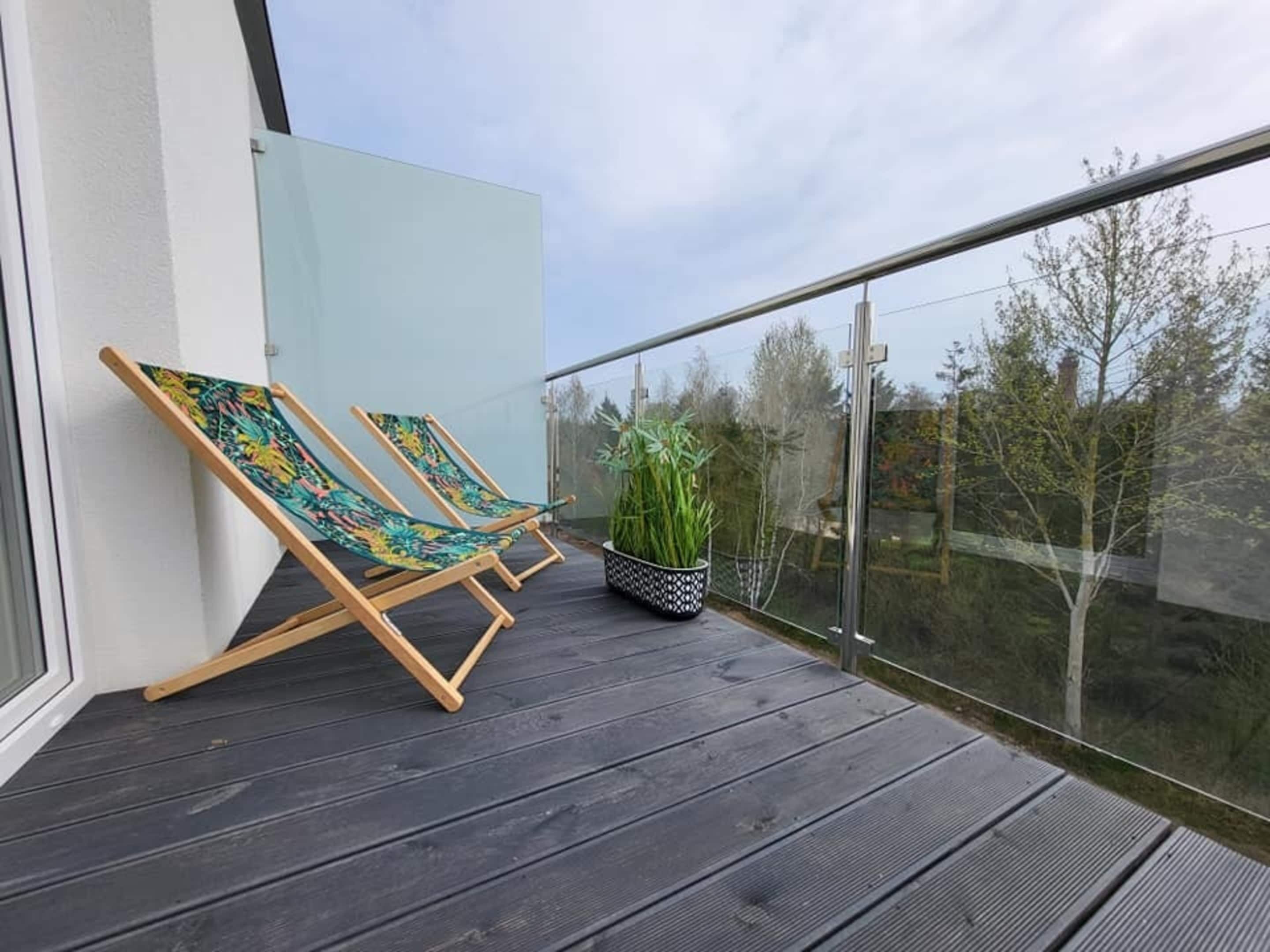 A balcony with two wooden lounge chairs and a potted plant.