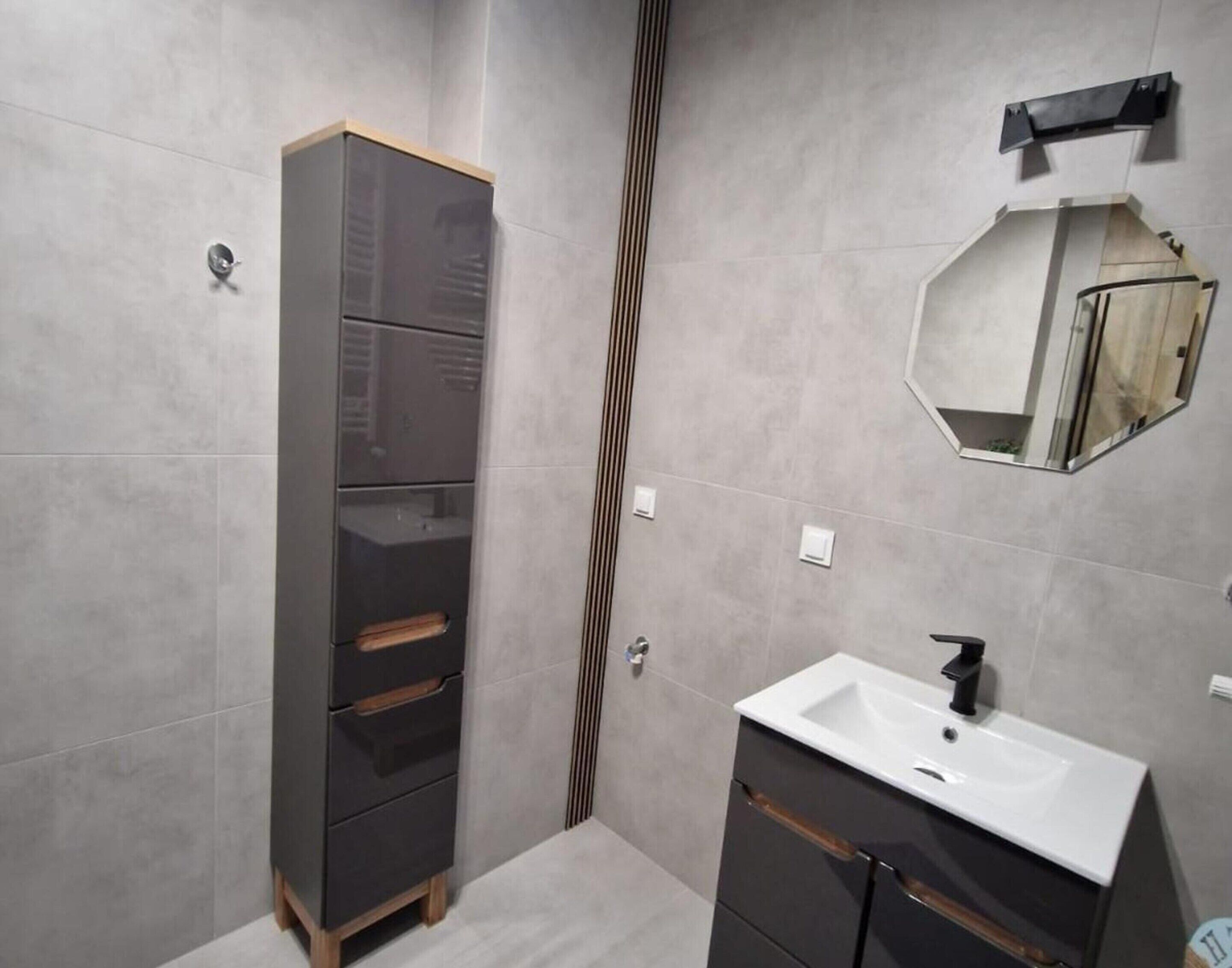 A modern bathroom with a dark cabinet, a white sink, and a mirror.