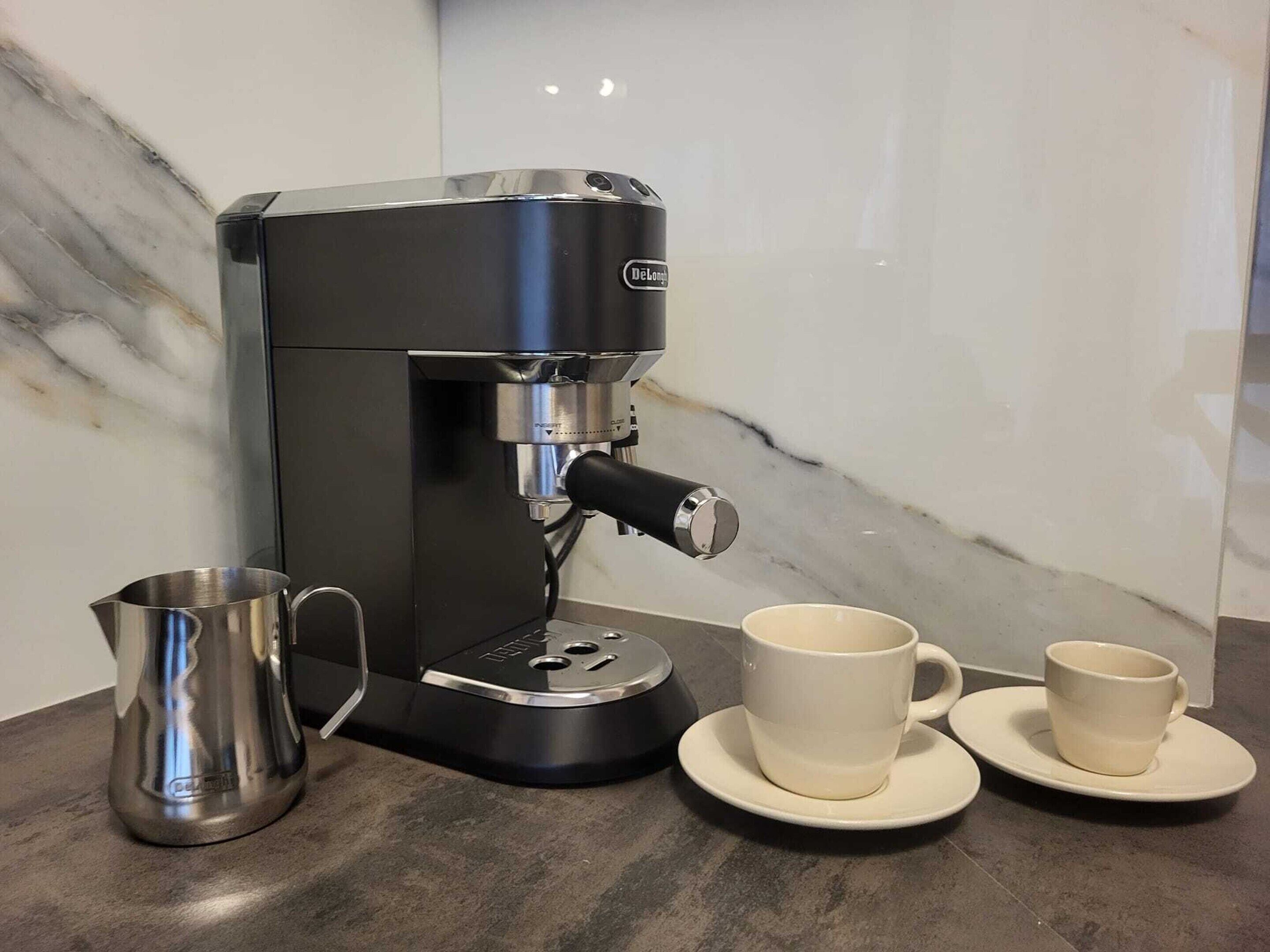 A coffee machine with a portafilter, a stainless steel pitcher, and two white cups on saucers.