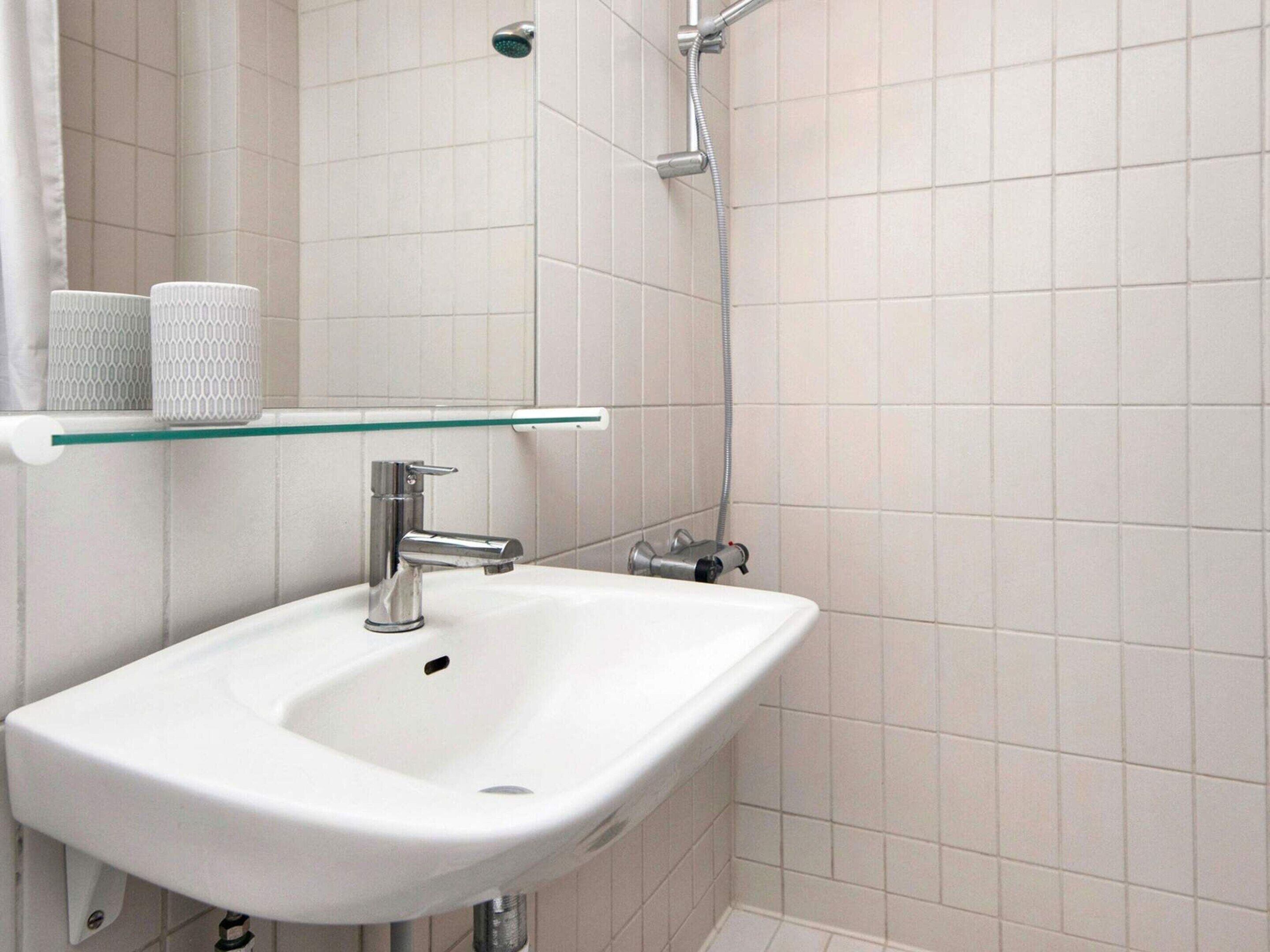 A bathroom with a white sink, a glass shelf, and a shower.