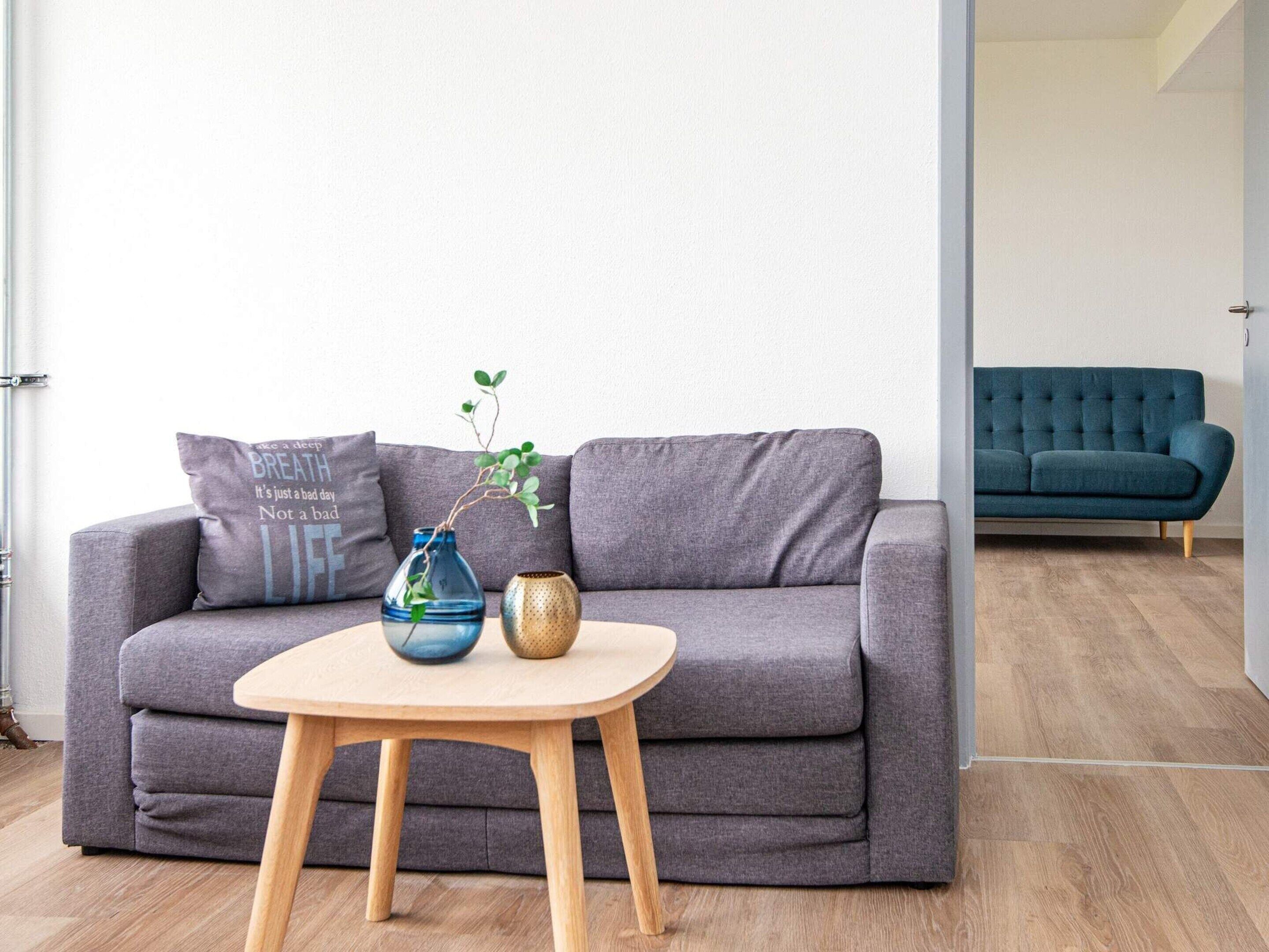 Una sala moderna con un sofá gris, una mesa redonda de madera y dos jarrones.