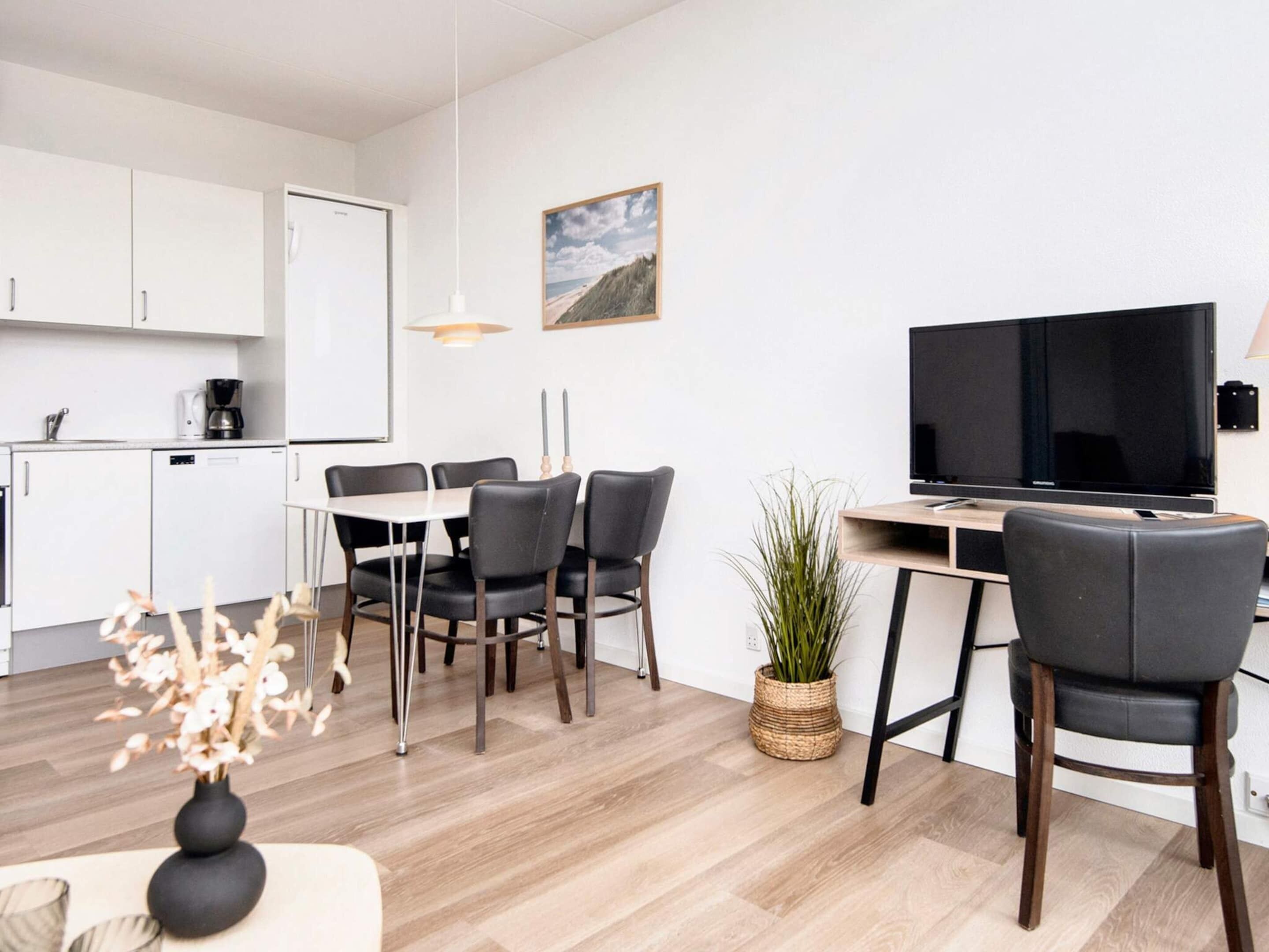 Une pièce moderne et bien éclairée, comprenant une table à manger, des chaises, un téléviseur et un coin cuisine.