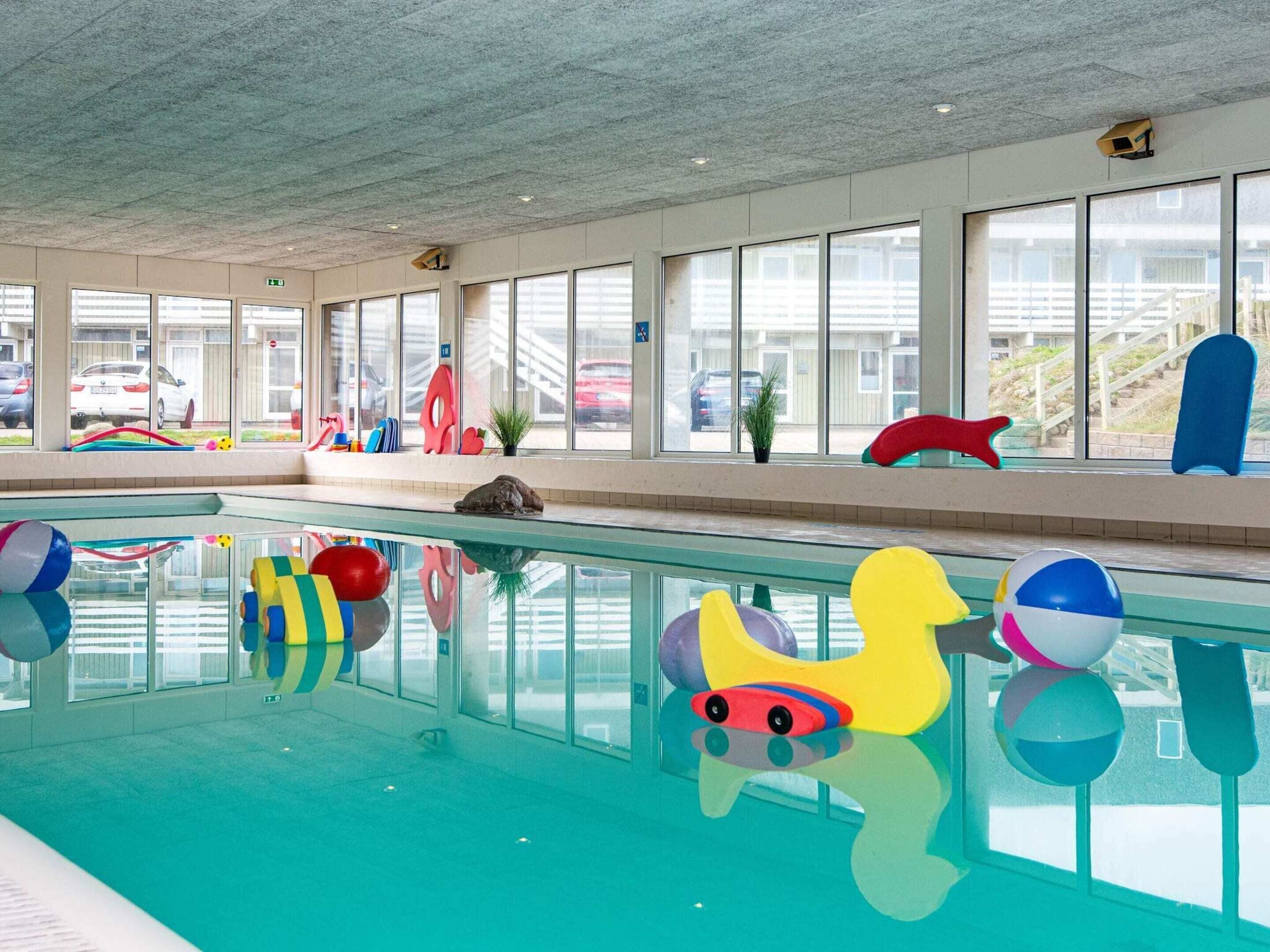Piscina interna com equipamentos de recreação coloridos e amplas janelas.