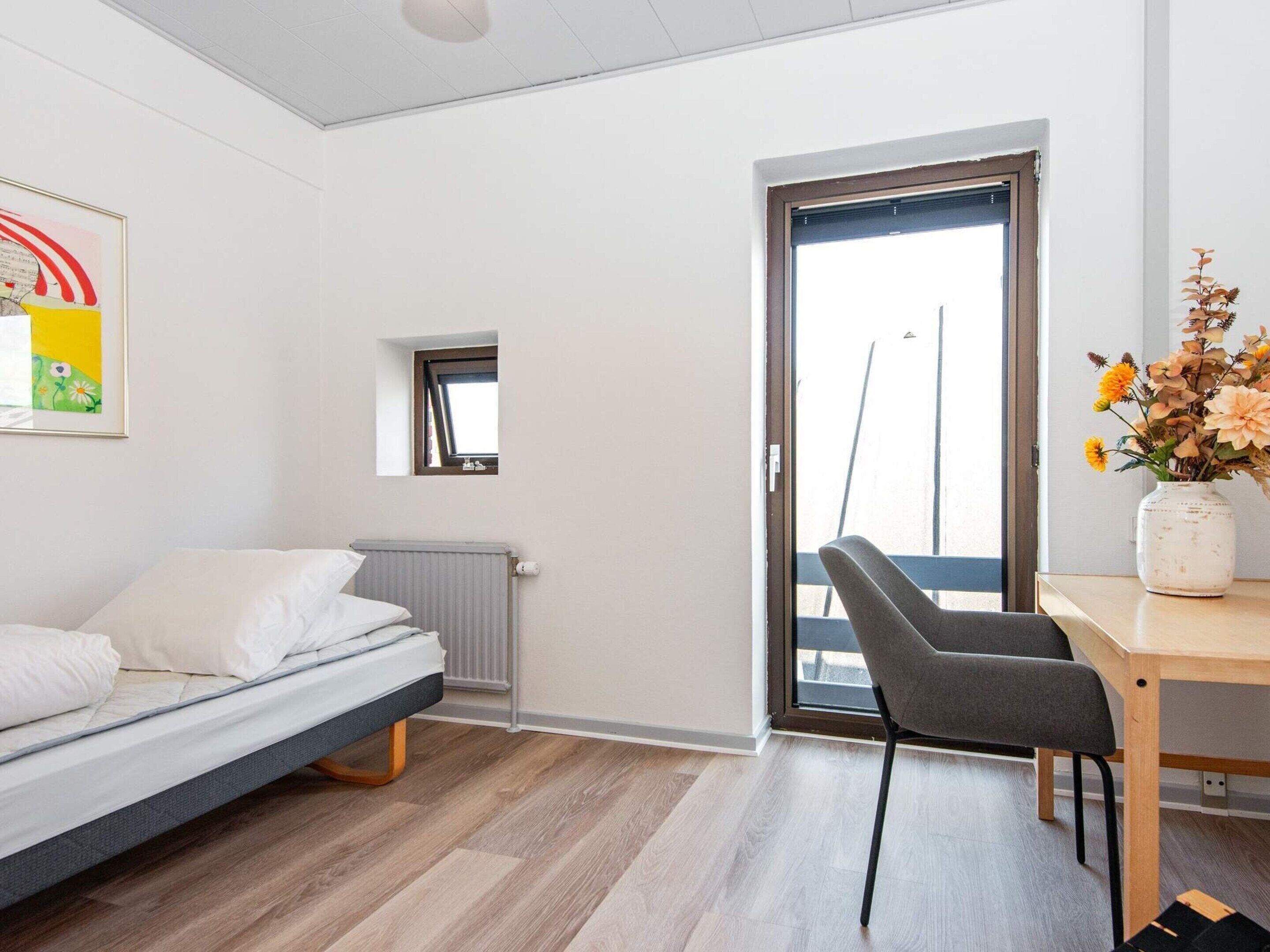 Un dormitorio moderno con cama, una ventana pequeña, un radiador y un escritorio con silla.
