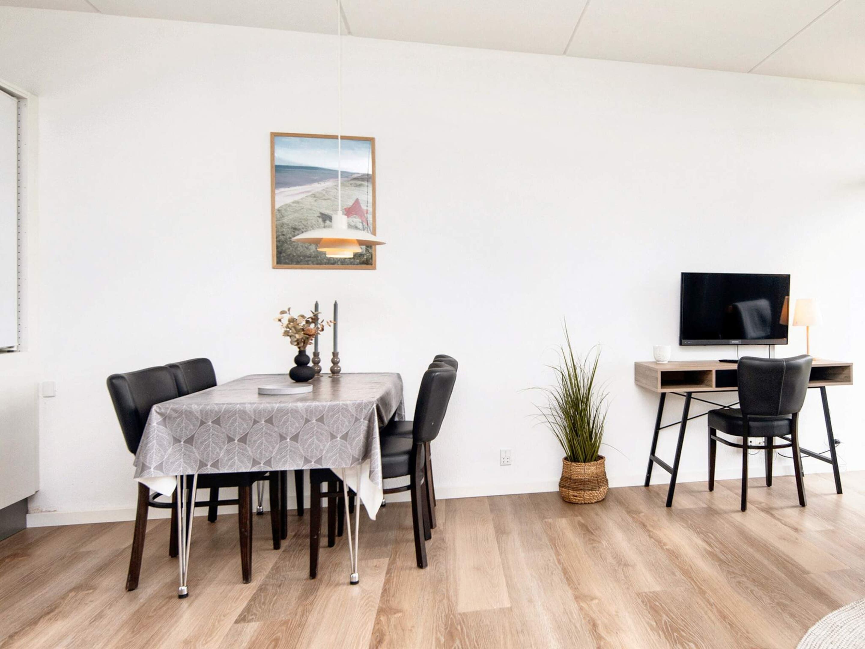 Un espace repas moderne avec une table dressée pour quatre personnes, un téléviseur posé sur un bureau et un tableau encadré accroché au mur.