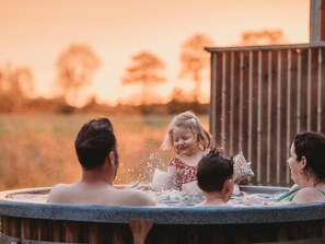 A family enjoying a hot tub with a wooden deck and a natural landscape in the background. - Atmospheric Lodge With Unobstructed View, Located in Beautiful Drenthe (Ruinerwold)