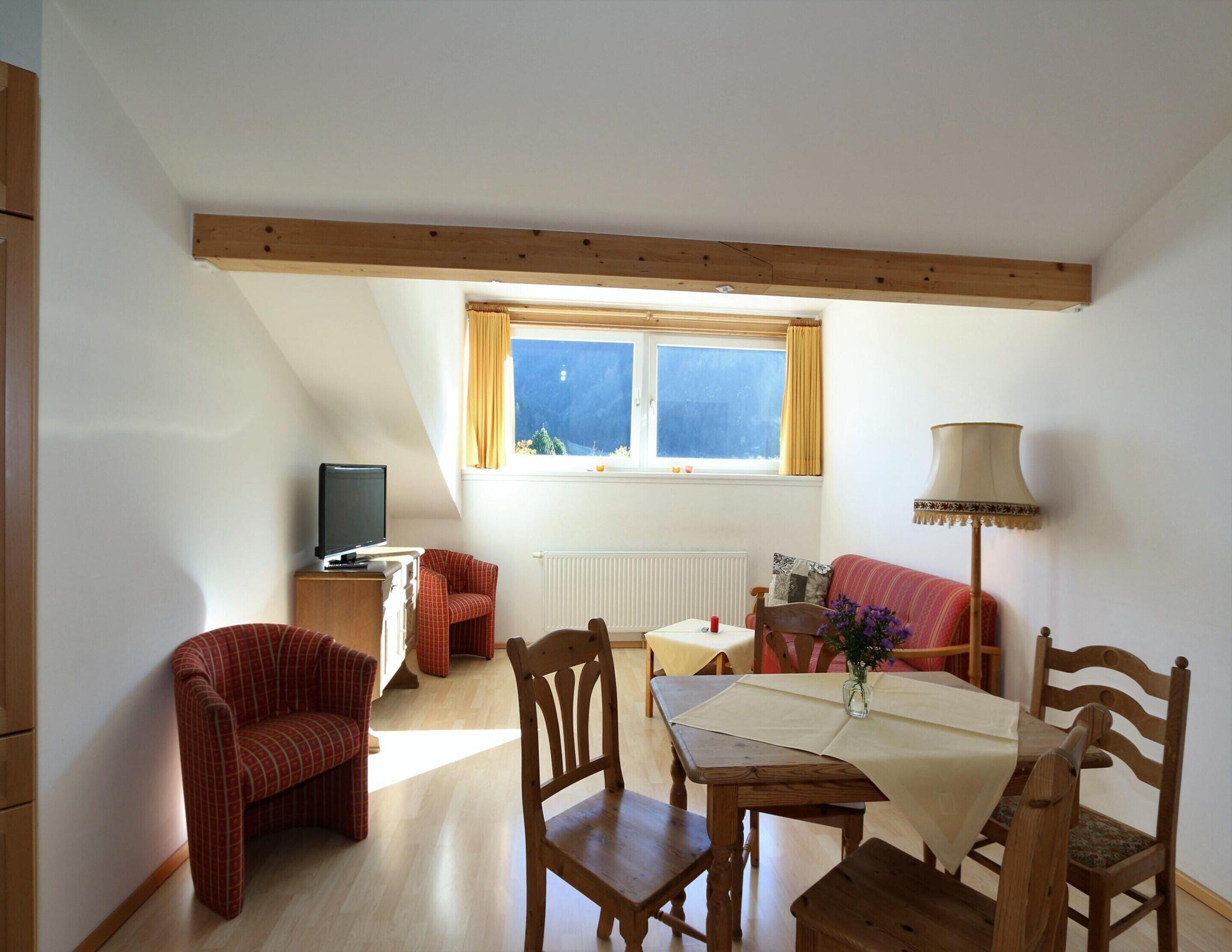 A cozy room with a dining table, chairs, a sofa, a TV, and a window with curtains.