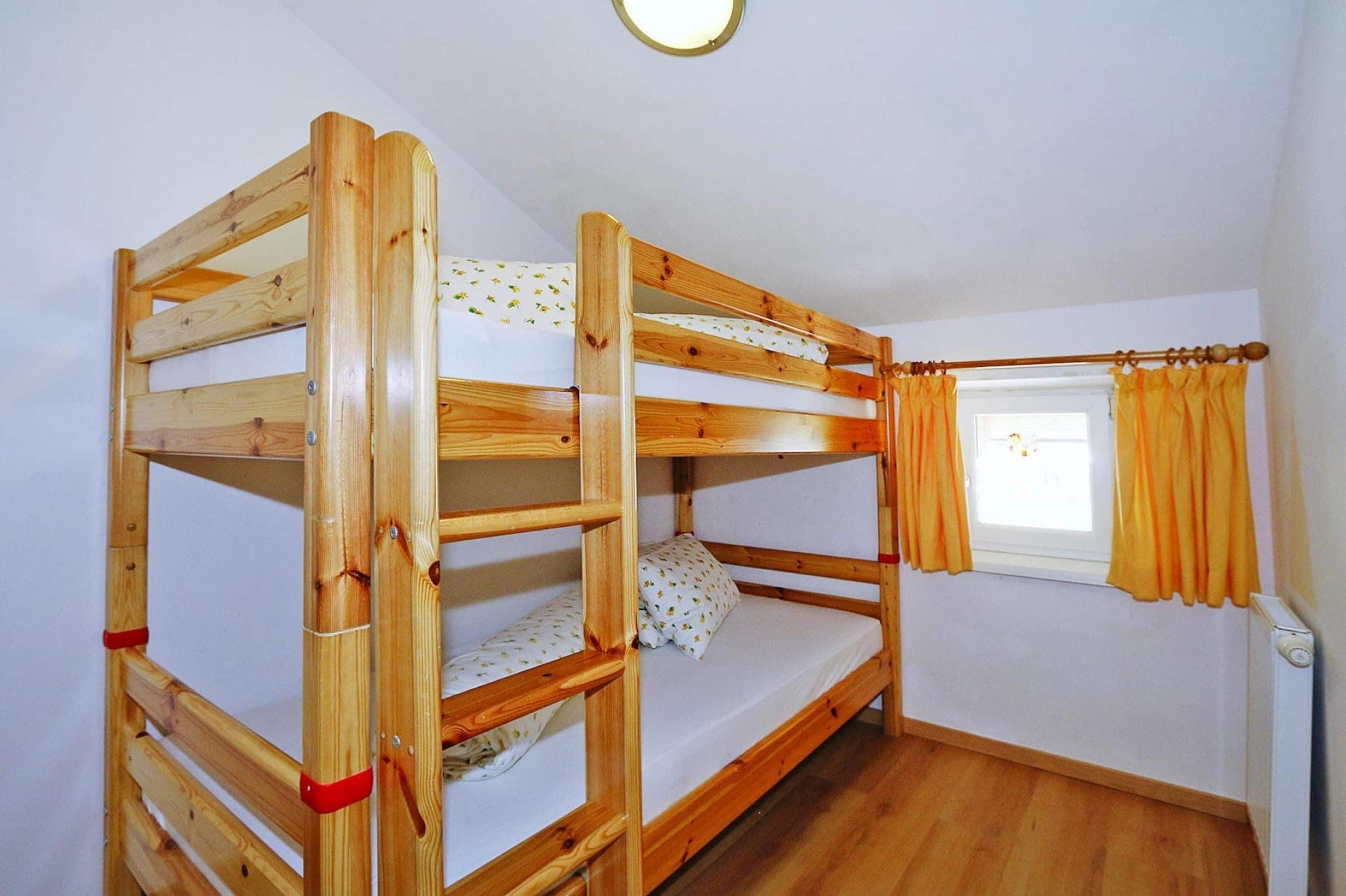 A bunk bed with two levels, a window with curtains, and a radiator on the wall.