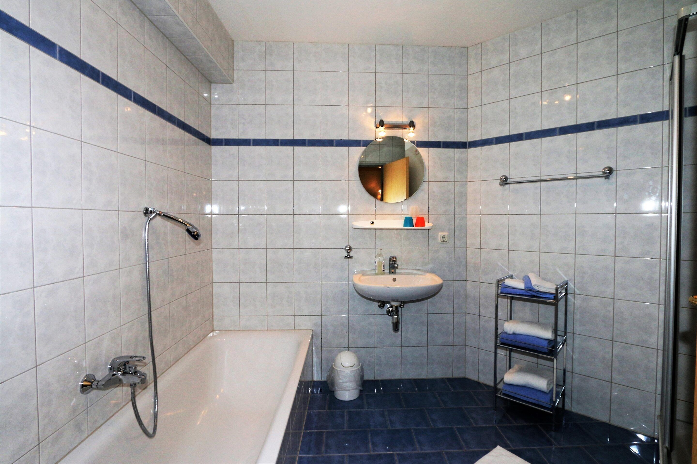 A bathroom with a bathtub, a sink, a mirror, and a towel rack.