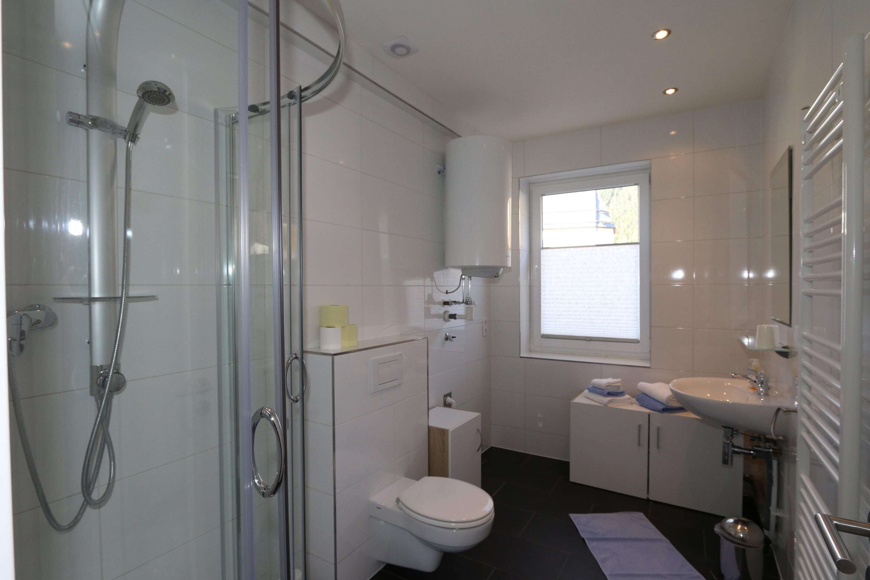 Een moderne badkamer met een douchecabine van glas, een toilet, een wastafel en een raam voor natuurlijk licht.