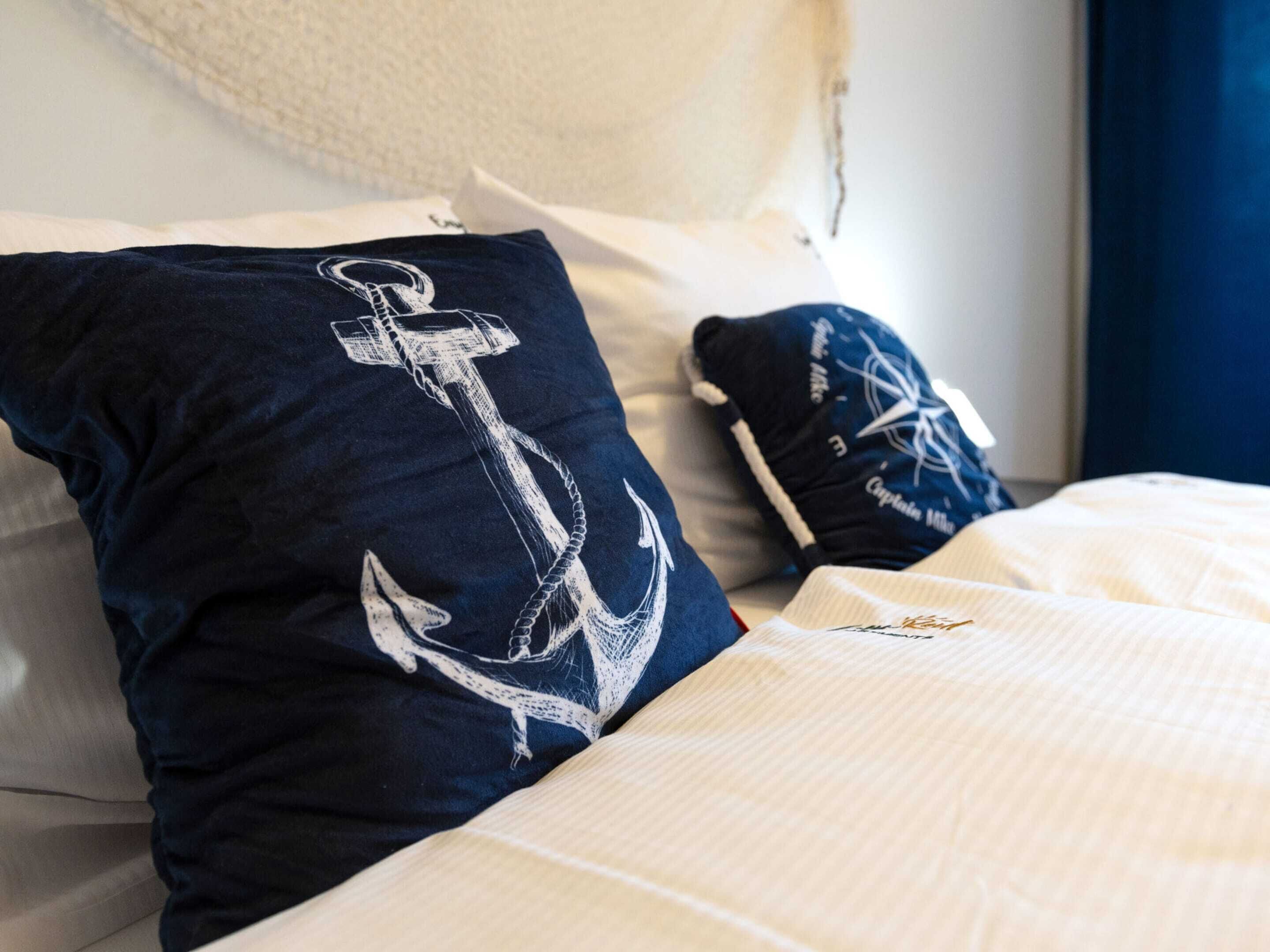 A bed with navy blue pillows featuring white anchor designs, a white comforter, and a navy blue pillow with a compass design.