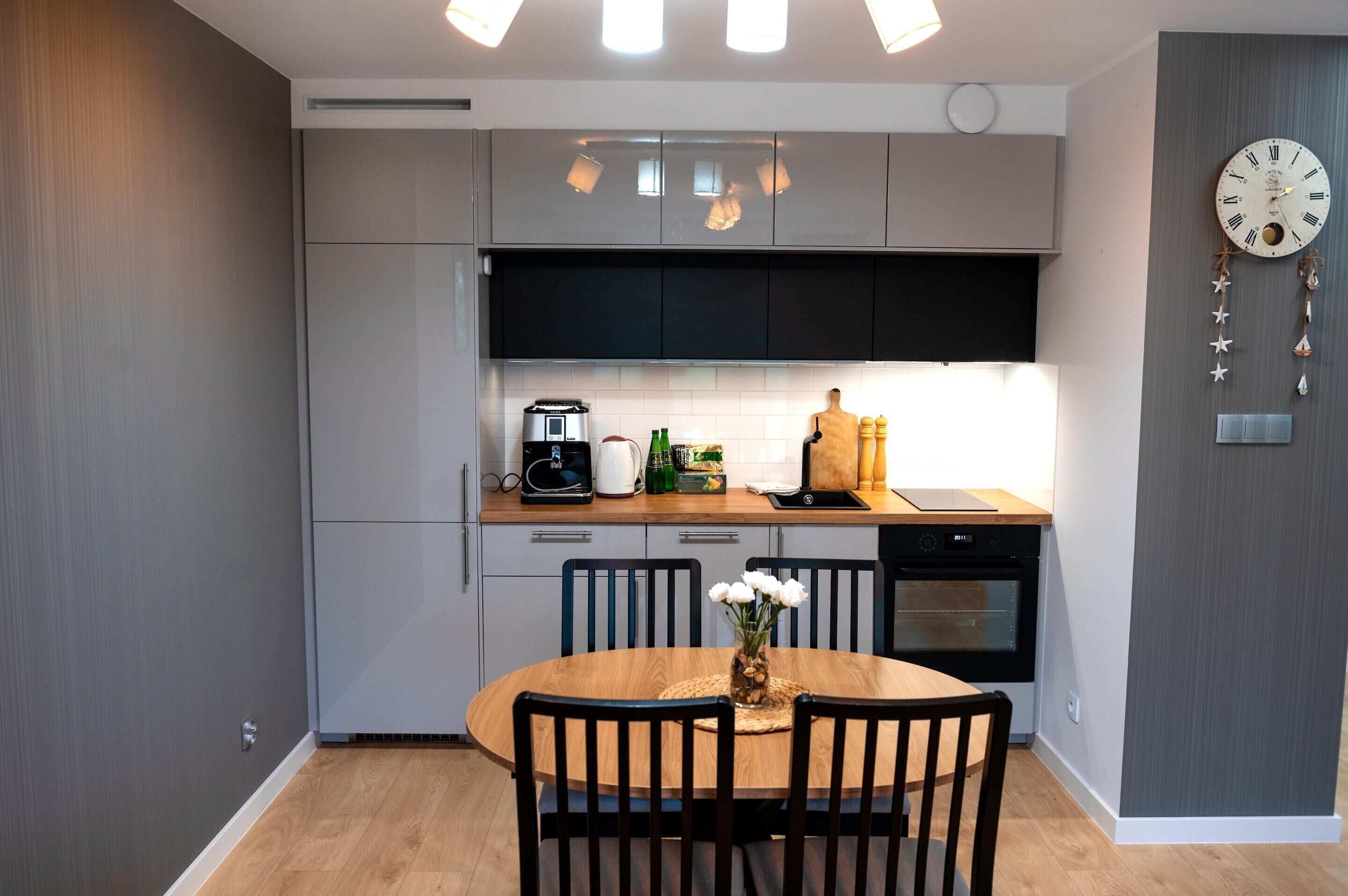 A modern kitchen with grey cabinets, a wooden dining table, and a clock on the wall.