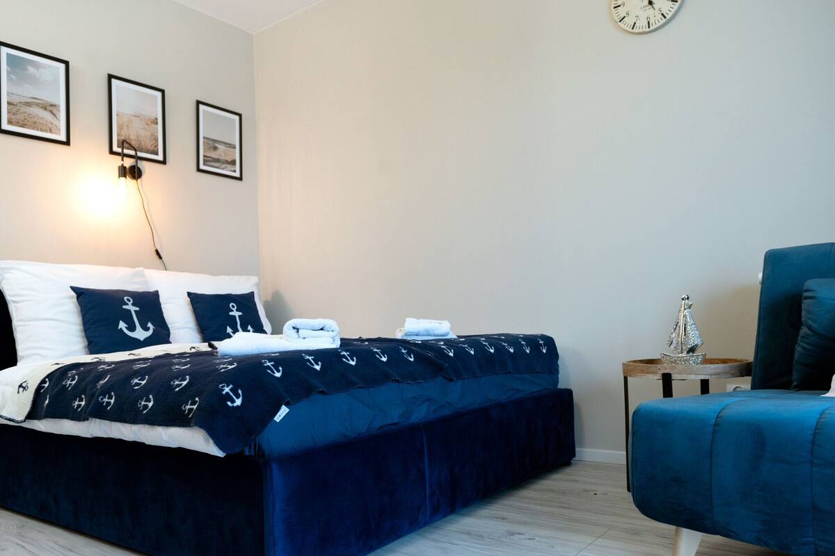 Quarto bem arrumado com cama, cadeira e mesa de cabeceira.