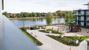Ein Park am Flussufer mit Spielplatz, Bänken und einem modernen Gebäude mit Balkonen.