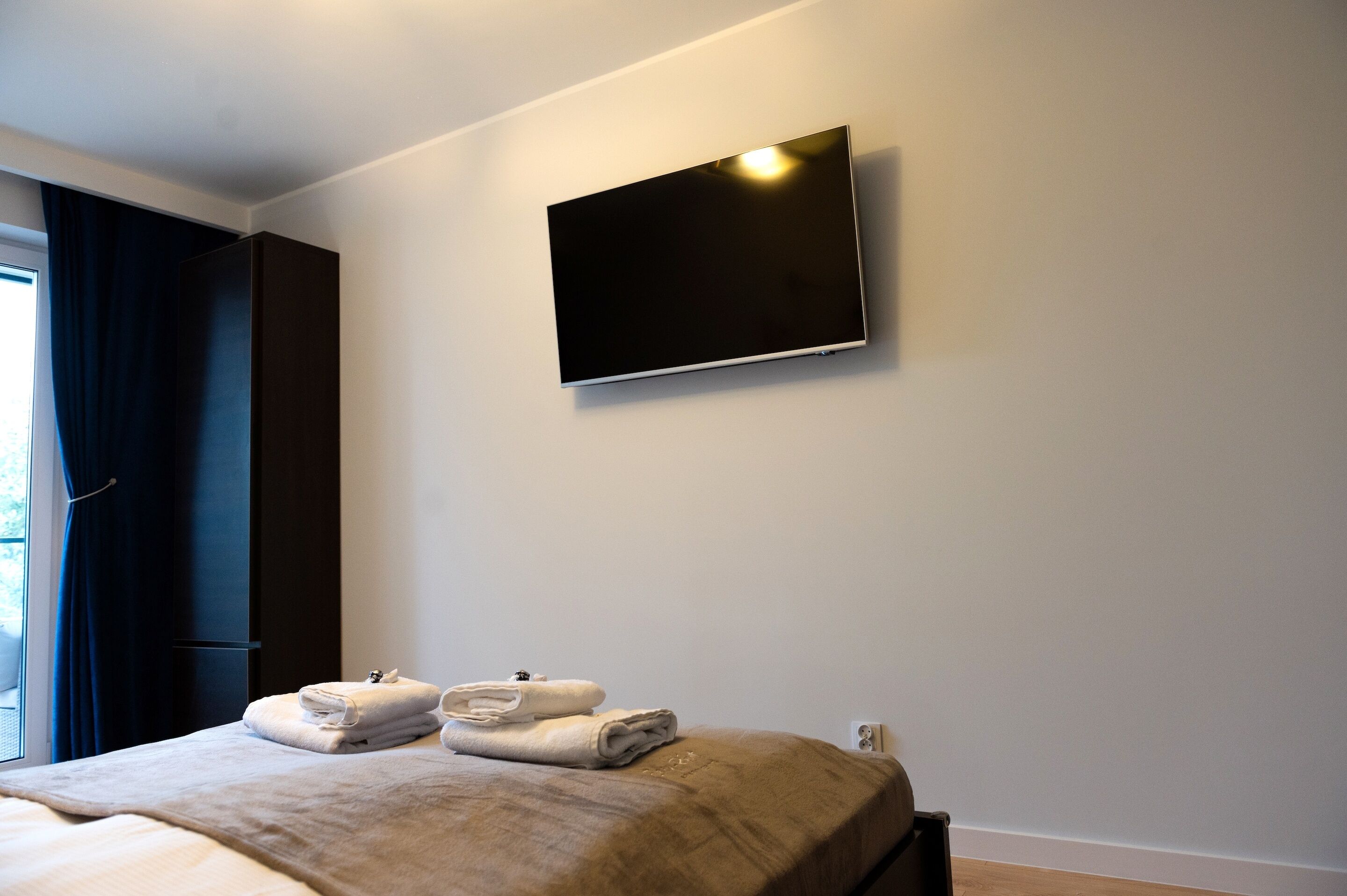 Quarto de hotel com cama, televisão de tela plana na parede e janela com cortinas.