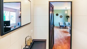 Ein modernes Badezimmer mit einem großen Spiegel, einem schwarzen Waschbecken und einem Holzboden, der in einen Wohnbereich mit einer Couch und einer Lampe führt.