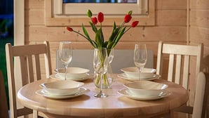 A wooden dining table with white plates and empty wine glasses, set against a wooden wall with a window overlooking a building. - New Holiday Homes for 2 People in Dziwnowek (Kamien Pomorski)