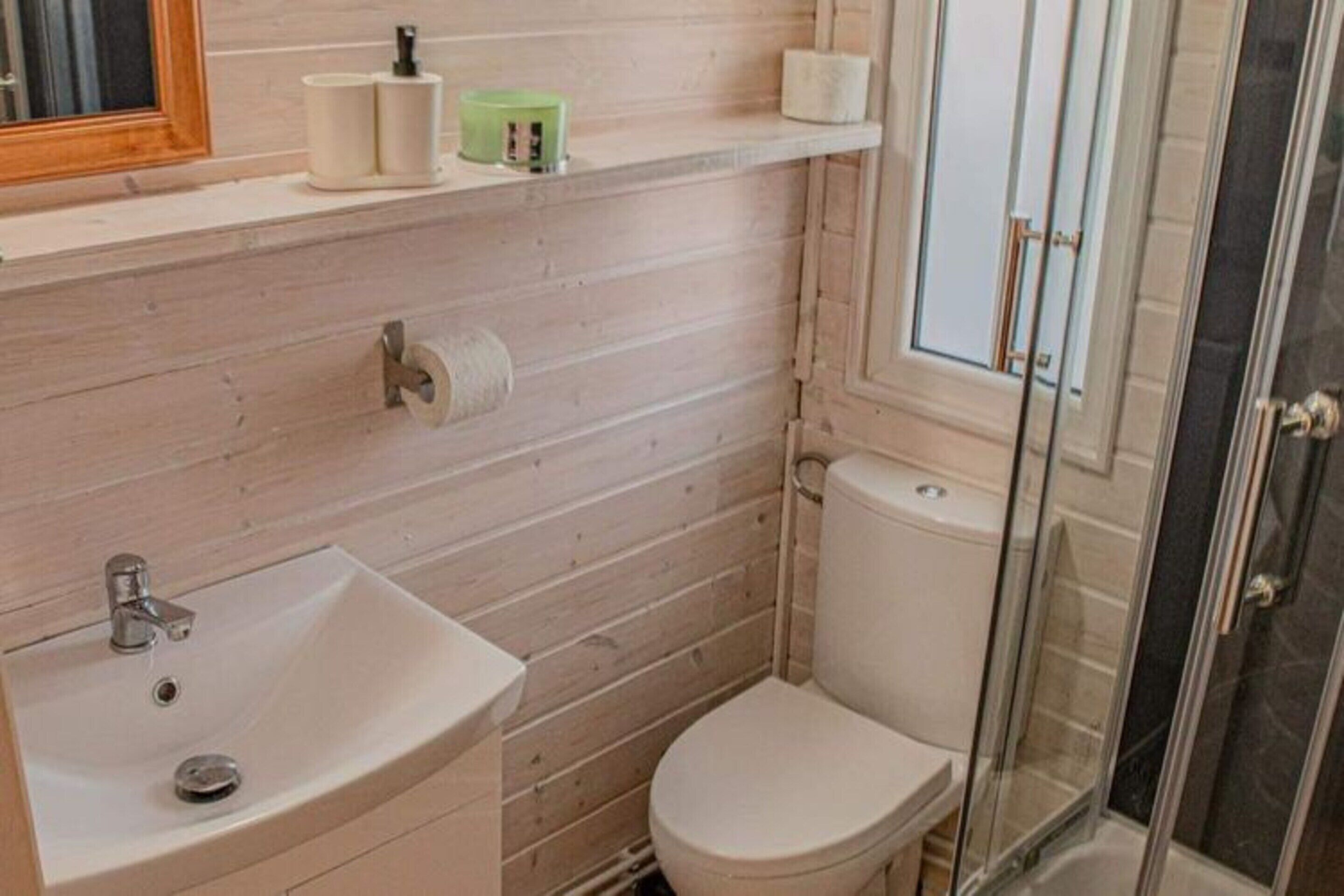 A bathroom with a wooden wall, a white sink, a toilet, and a glass shower enclosure.