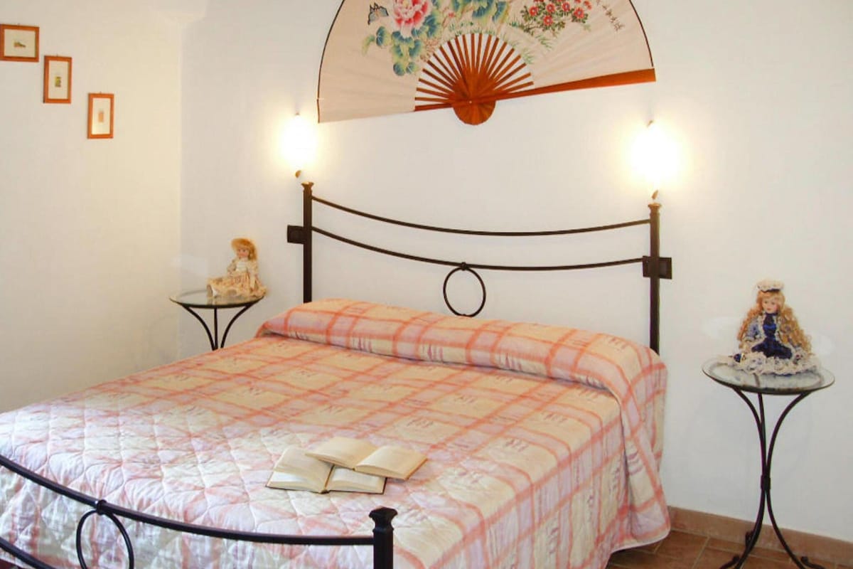 A bedroom with a bed, two bedside tables, a hanging fan, and a wall-mounted light fixture.